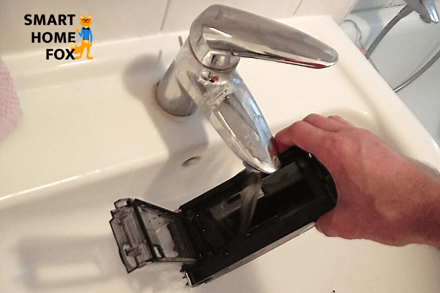 The mobile dust container of an iRobot Roomba vacuum robot is washed out under running water.